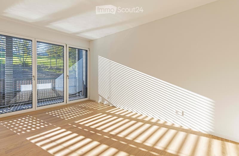 Empty room with wooden floor, white walls, sliding glass doors leading to a balcony, trees view