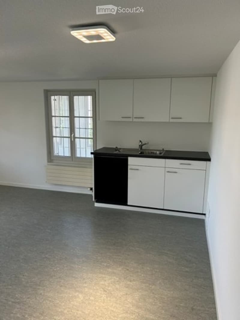 Empty kitchen with white cabinets, black countertop, sink, and a window with frosted glass panels. No furniture or appliances are present.