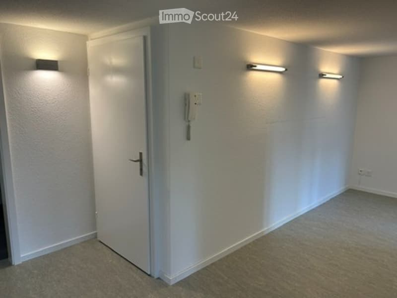 Empty room with white walls, carpeted floor, and a single door. No furniture or equipment is present.