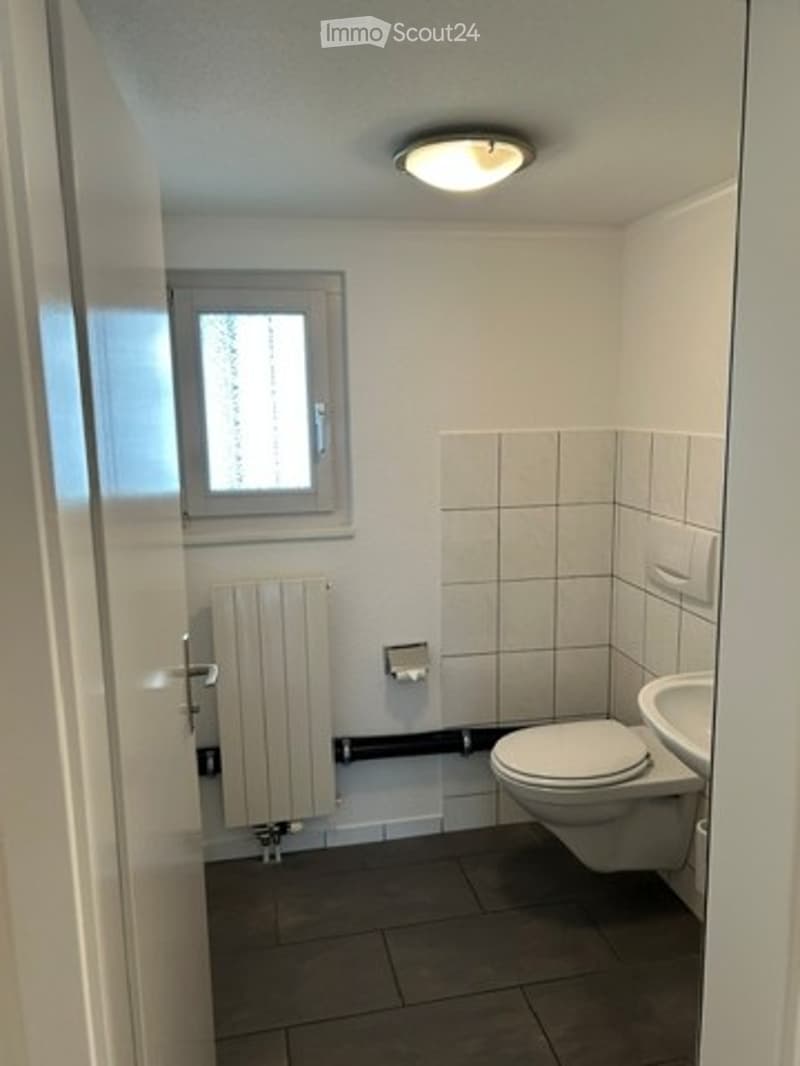 Small bathroom with white tiled walls, a toilet, a sink, a radiator, and a window providing natural light.