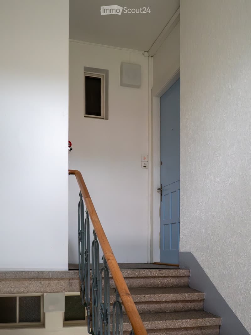 Staircase with wooden handrail and metal balustrade, leading to a closed door at the top.