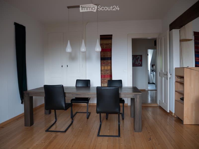 Dining room with a wooden table, four black chairs, pendant lights, and a view into the kitchen area.