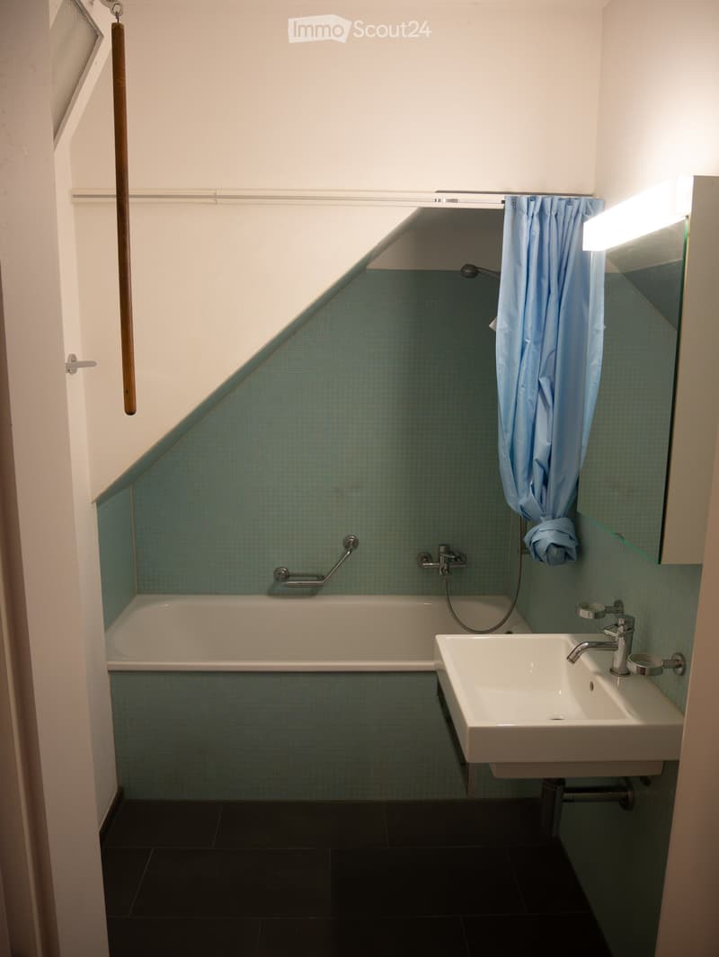 Modern bathroom with a bathtub, sink, and mirror. Features blue tiled walls and a shower curtain.