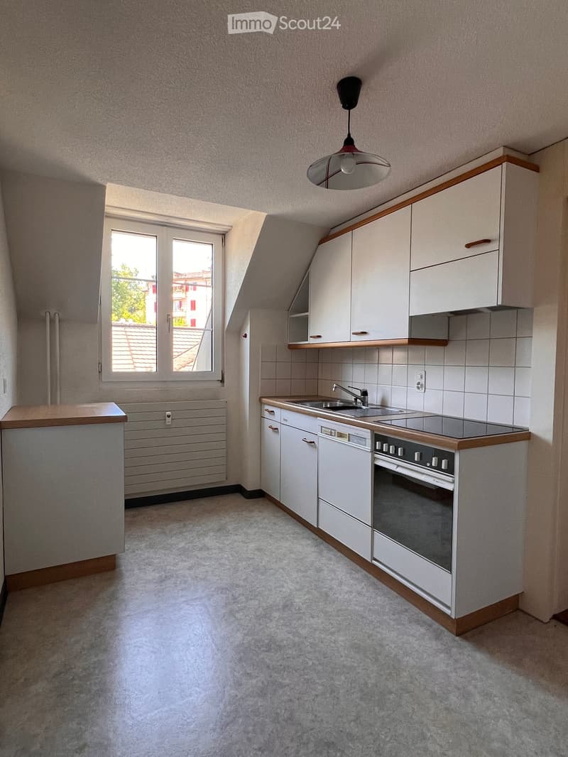 Modern kitchen with white cabinets, a sink, oven, dishwasher, and a window offering a view of the roof and surrounding buildings.