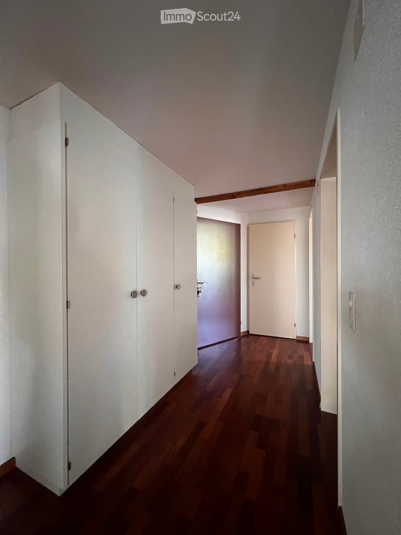 Empty hallway with wooden flooring, white walls, and several closed doors.