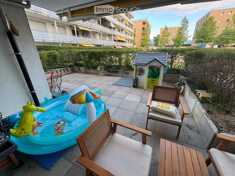 Balcony area with a small inflatable pool, wooden chairs, a small table, a toy house, and a bicycle.