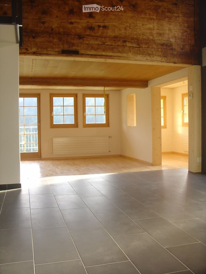 Empty room with wooden beams on the ceiling, large windows, and tiled floor. No furniture or equipment present.
