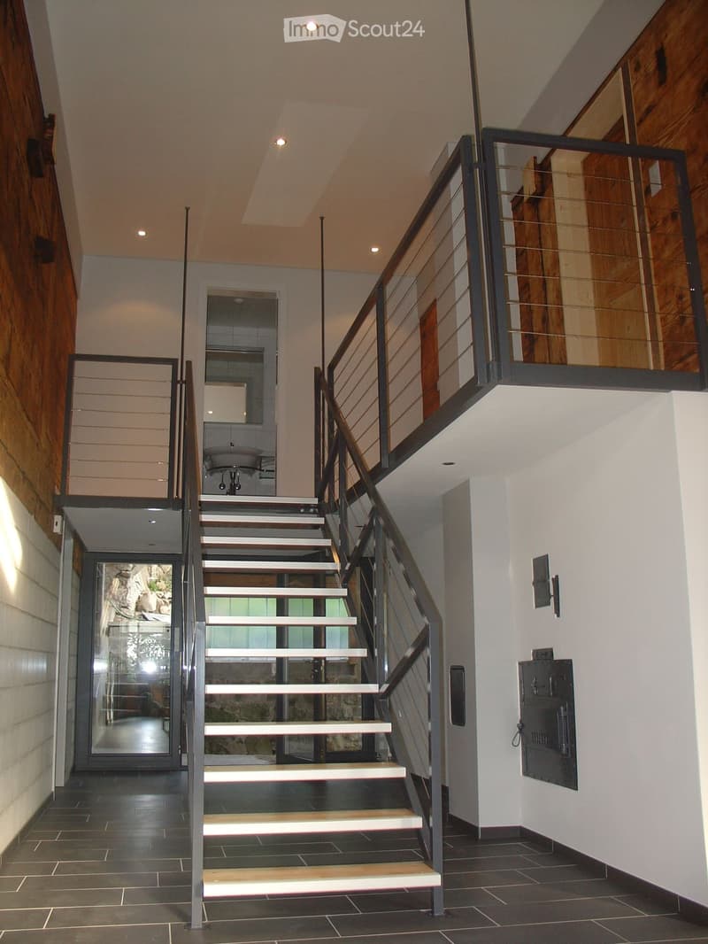 Modern interior staircase with wooden steps, metal railing, and glass panels, leading to a room with a sink visible in the background.