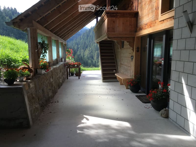 Balcony with wooden staircase, stone wall, potted plants, and scenic mountain view.