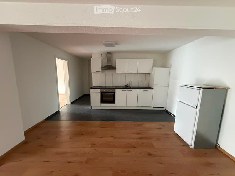 Modern kitchen with white cabinets, stainless steel appliances, and a black countertop. The space features wooden flooring and a small bar area with a refrigerator.