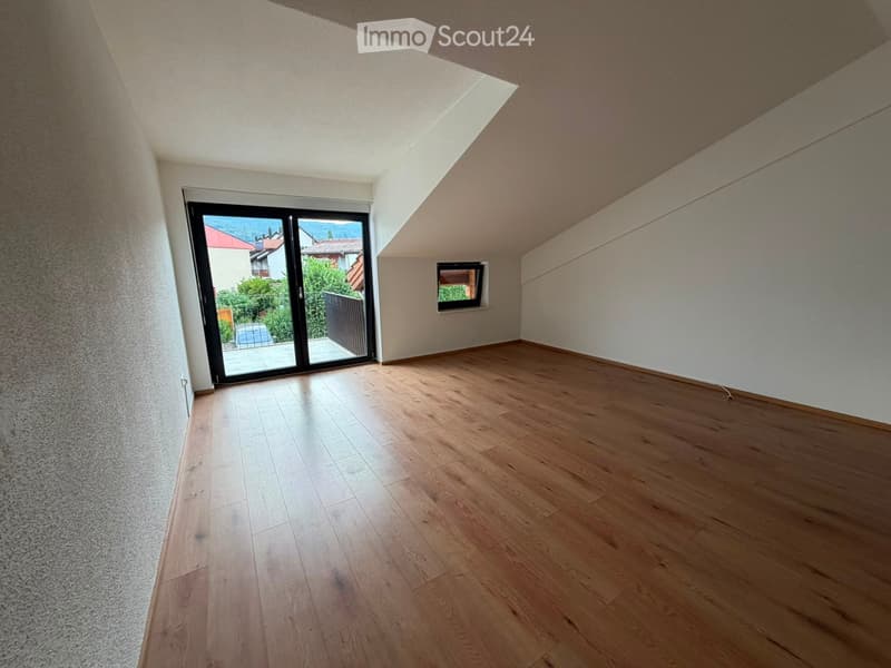 Empty room with wooden flooring, large sliding glass door leading to a balcony, and a small window on the side wall.