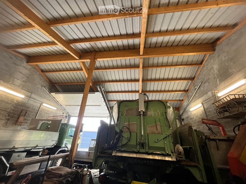 {"type": "Garage", "objects": ["truck", "machinery", "table", "stool"], "description": "Garage with exposed wooden beams and corrugated metal roof, containing a green truck, machinery, and a small table with a stool.", "localized_descriptions": {"EN": "Ga