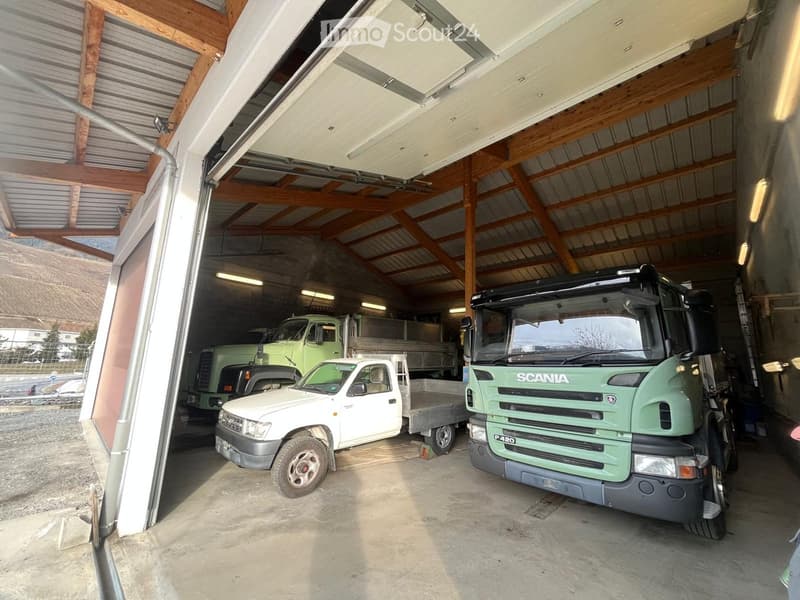 Garage with three vehicles: a green Scania truck, a white pickup truck, and a green truck, with wooden beams and a partially open garage door.