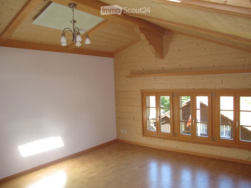 Empty room with wooden walls, exposed wooden beams, large windows, and a chandelier.