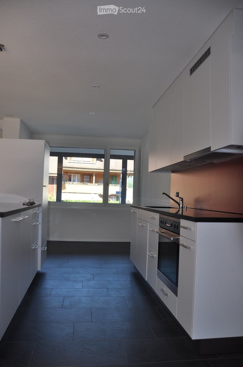 Modern kitchen with white cabinets, dark countertops, and a built-in oven. Features a large window with a view of the outside.