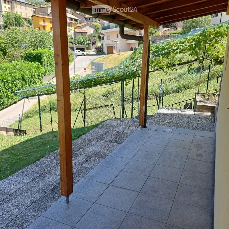 Balcony with tiled floor, wooden beams, metal railing, and a view of a residential area with greenery and houses.