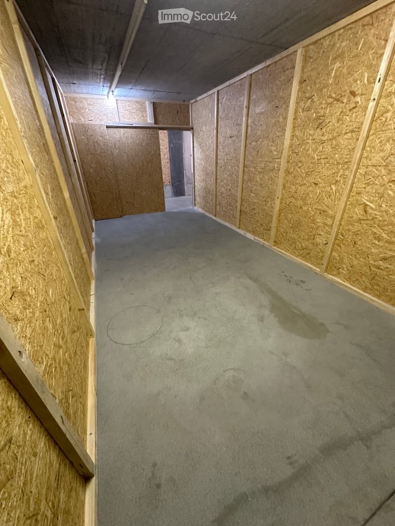 Empty room with unfinished wooden walls and a concrete floor, showing construction marks and a doorway leading to another space.