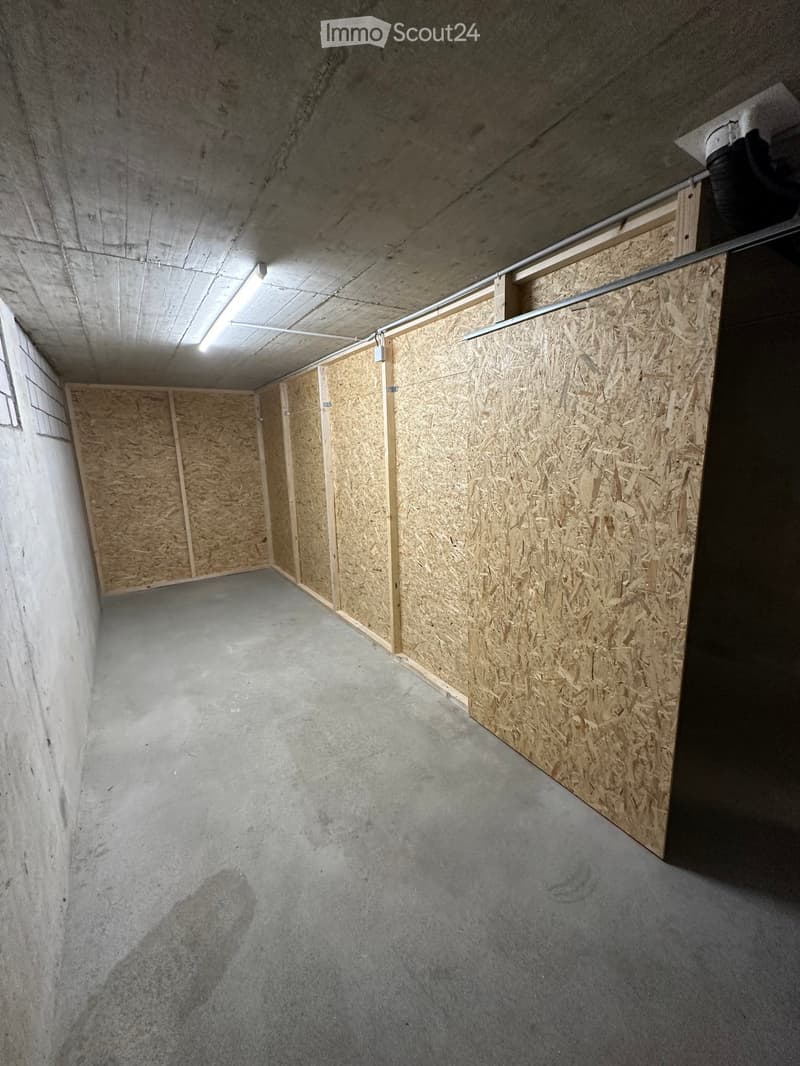 Empty room with concrete walls and floor, wooden paneling on one side, and fluorescent lighting.