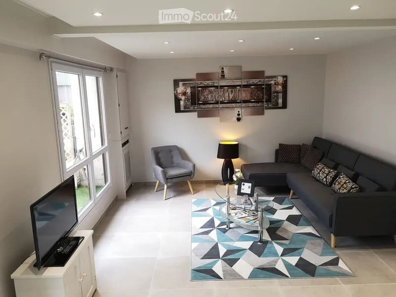 Modern living room with a grey sectional sofa, armchair, glass coffee table, floor lamp, and a geometric patterned rug.
