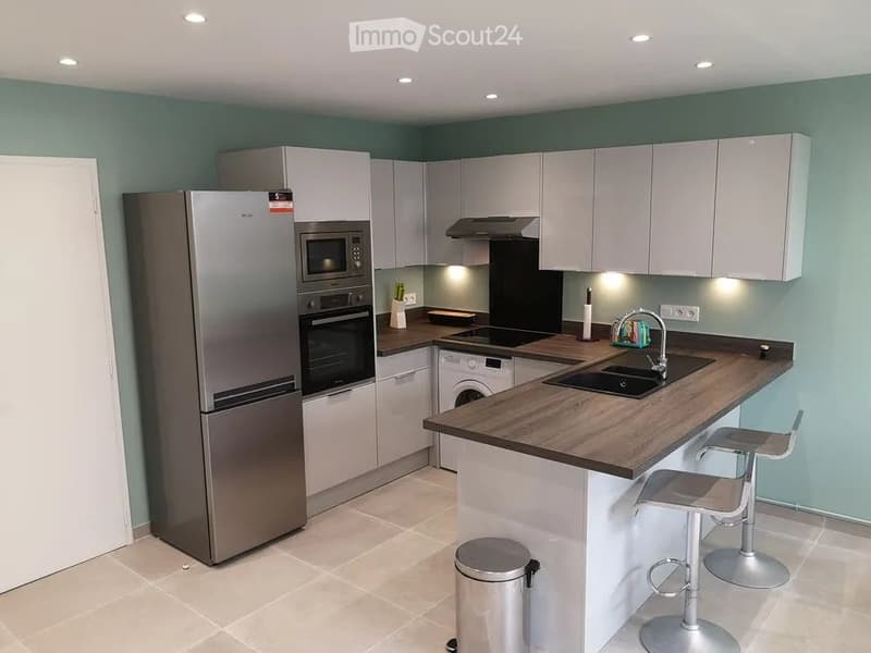 Modern kitchen with light grey cabinets, stainless steel appliances, wooden countertop, and two bar stools.