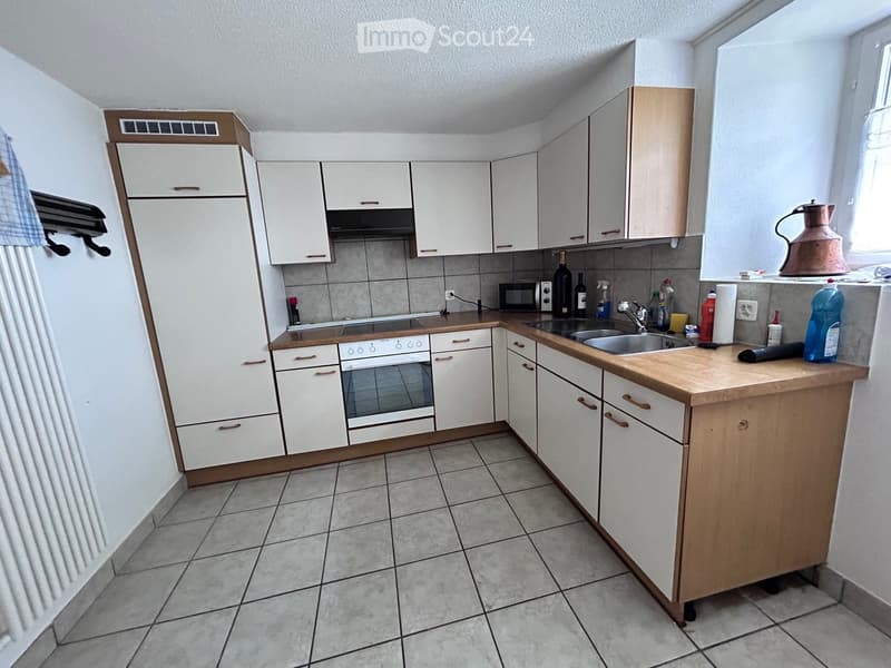 A compact kitchen with white cabinets, a wooden countertop, and tiled flooring. Visible appliances include an oven, microwave, and sink.