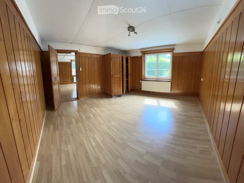 Empty room with wooden walls and flooring, a single window, and a door leading to another room.