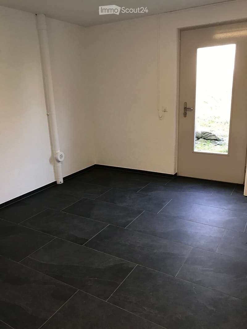 Empty room with black tiled floor, white walls, and a door leading outside.