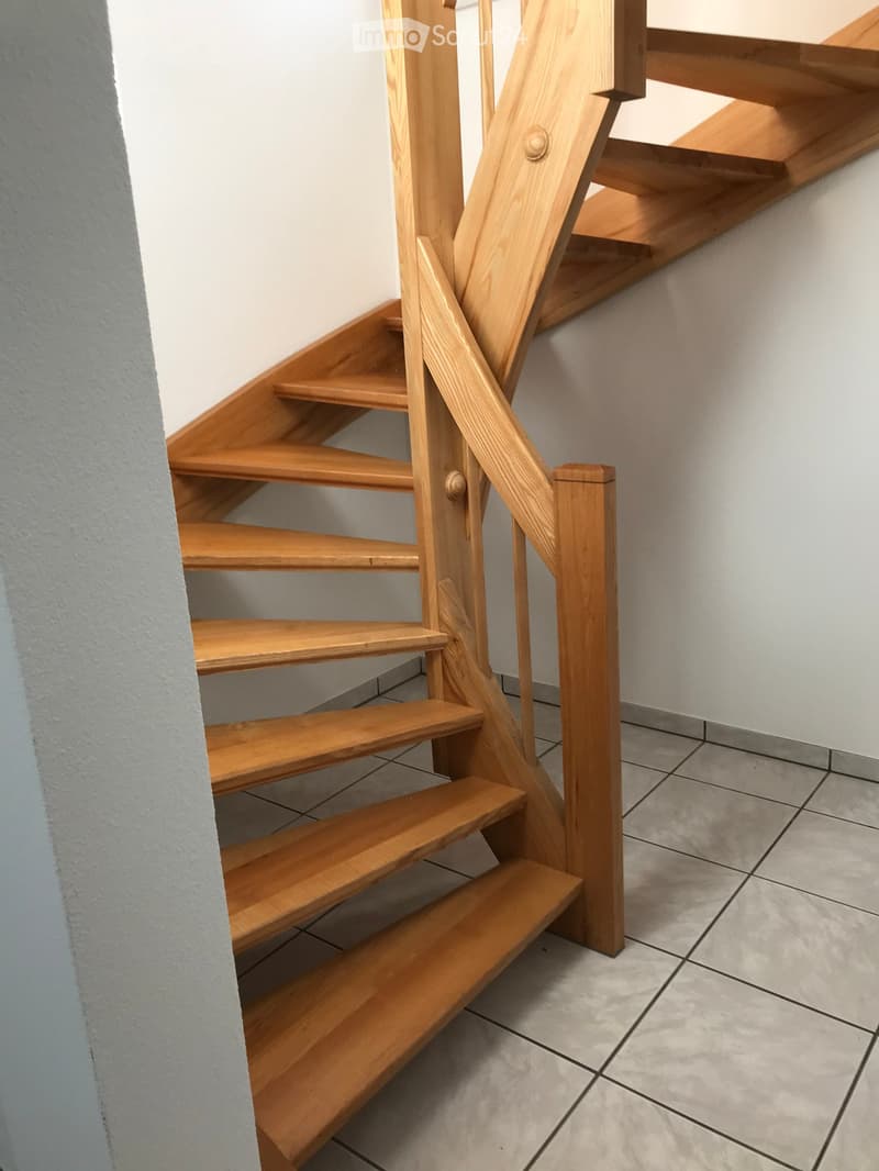 Wooden staircase with a handrail, light-colored walls, and tiled floor.