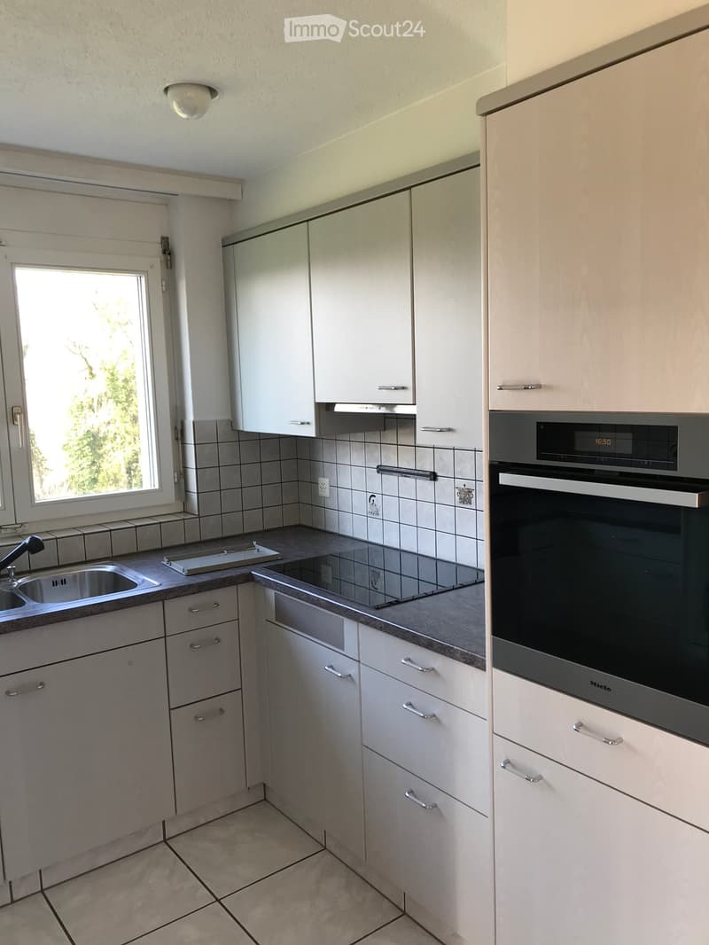 Modern kitchen with white cabinets, stainless steel sink, and built-in oven. Features tiled backsplash and tiled floor.