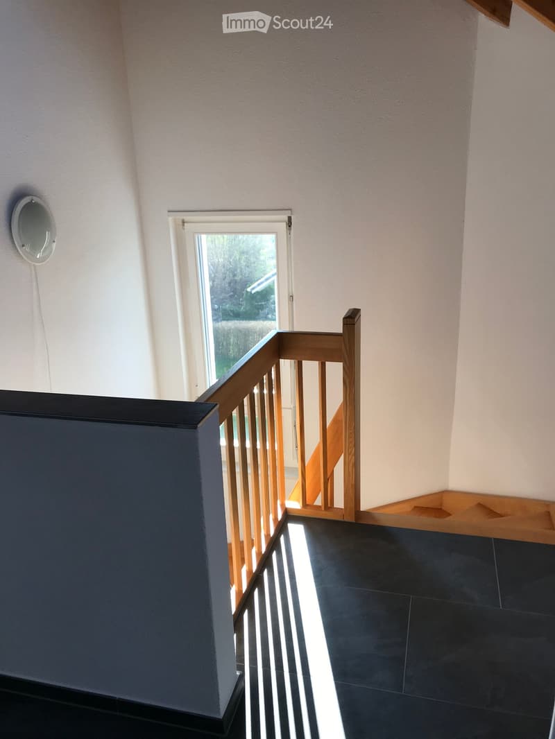 Modern hallway with dark tiled floor, wooden staircase railing, and a small window leading to an outdoor area.
