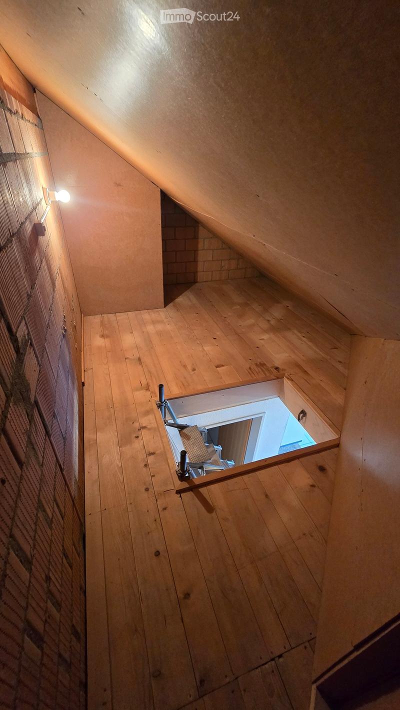 Wooden staircase with slanted ceiling and exposed brick wall, featuring a small opening to another room below.