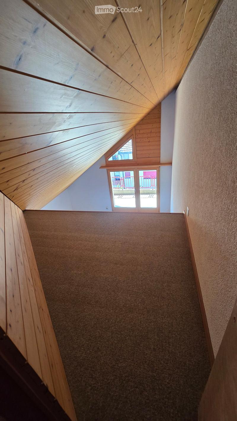 Carpeted staircase with wooden railings and slanted wooden ceiling, leading to a windowed landing area.