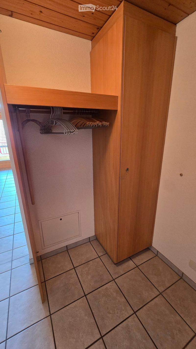 A narrow hallway with tiled flooring, wooden closet doors, and a built-in shelf with hanging space for clothes.