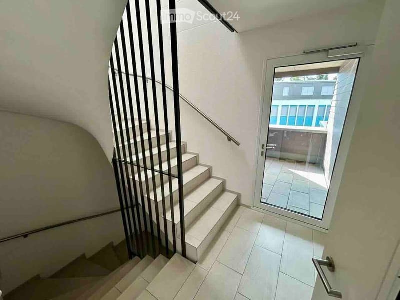 Modern hallway with tiled flooring, a staircase with a metal railing, and a glass door leading to an outdoor area.