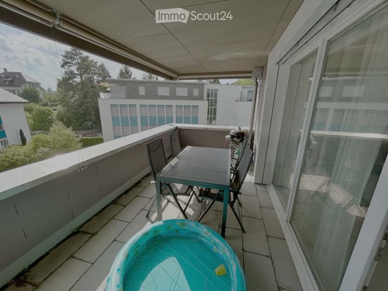 Balcony with tiled floor, table, chairs, and a small inflatable pool. Grill and outdoor furniture are visible.