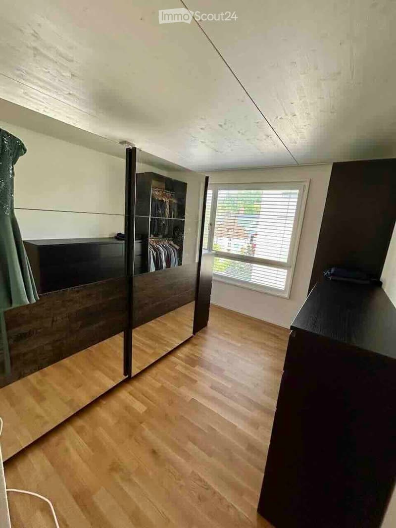 Spacious room with wooden flooring, large mirrored wardrobe, and a window with blinds.