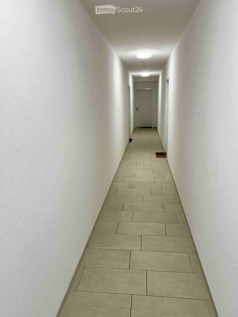 A long, narrow hallway with tiled flooring and white walls, leading to a closed door at the end.