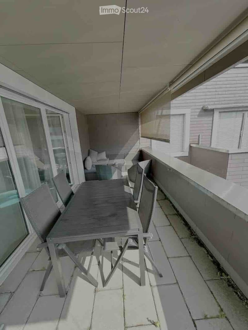 Balcony with a small table and chairs, enclosed by glass walls, with a view of the building exterior.