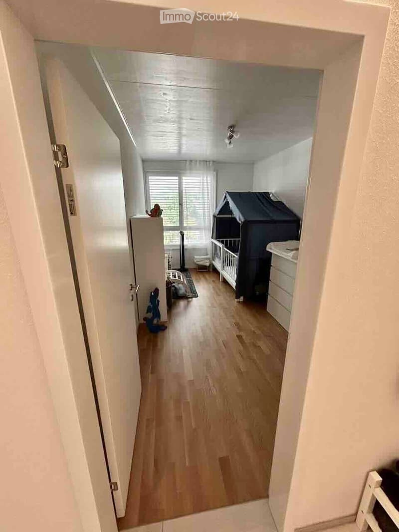 A well-lit children's room with wooden flooring, a crib, changing table, a small chair, and toys.