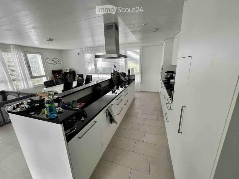 Modern kitchen with white cabinets, black countertops, and a central island. Features include a stove, microwave, fridge, and a dining area with chairs and a table.