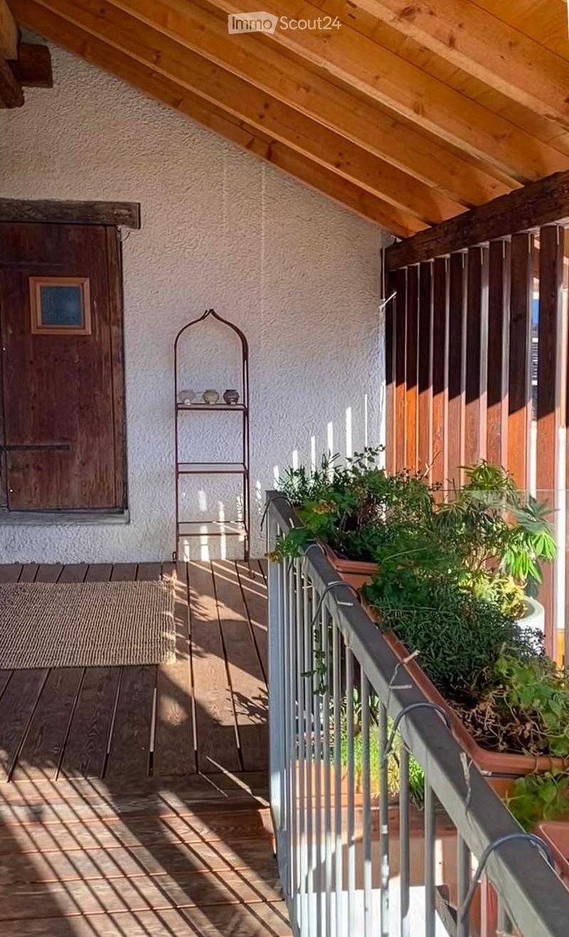 Balcony with wooden floor, metal railings, potted plants, and a small decorative shelf.