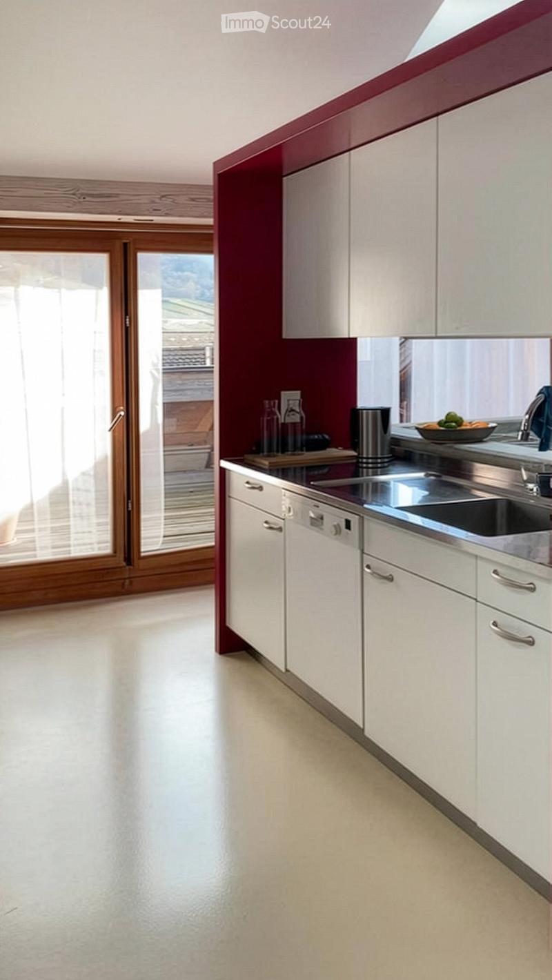 Modern kitchen with white cabinets, stainless steel sink, dishwasher, and a view through a large window.