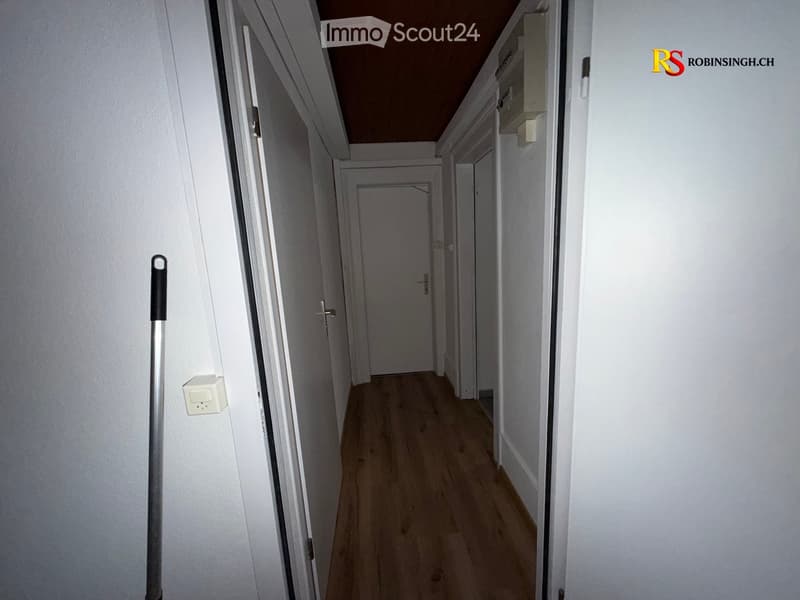 Empty hallway with wooden flooring, white walls, and several closed doors.