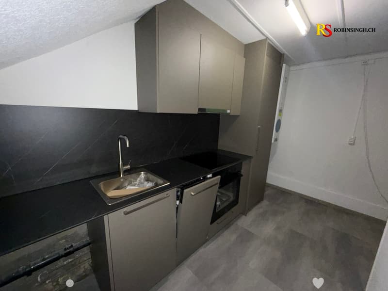 Modern kitchen with grey cabinets, black countertop, stainless steel sink, and built-in oven.