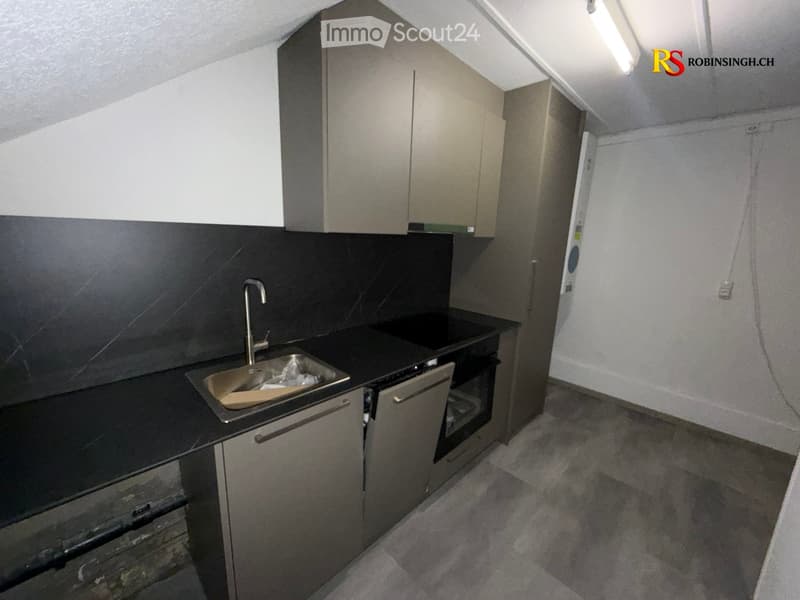 Modern kitchen with grey cabinets, black countertop, stainless steel sink, and built-in oven.