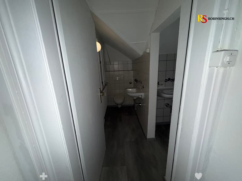 Two small bathrooms with tiled walls, a toilet, and a sink in each. The space is narrow with a slanted ceiling typical of an attic area.