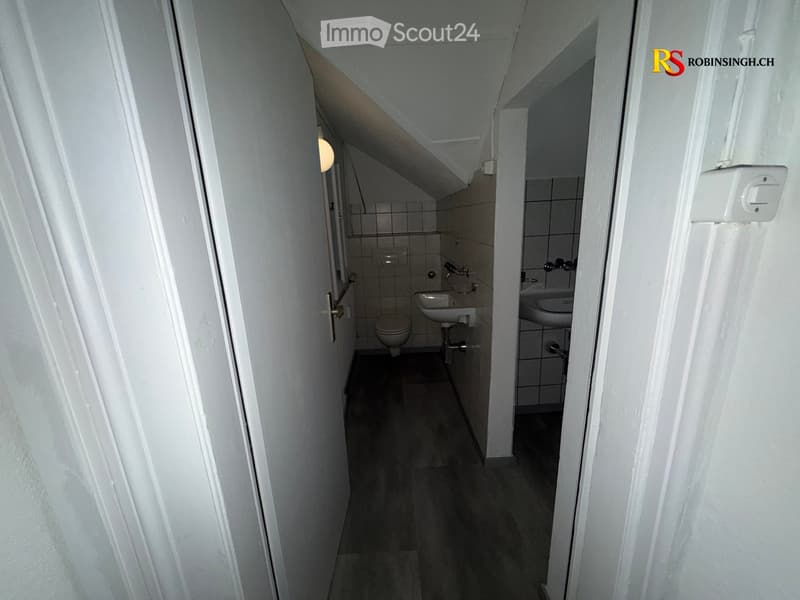 Two small bathrooms with tiled walls, a toilet, and a sink in each. The space is narrow with a slanted ceiling typical of an attic area.