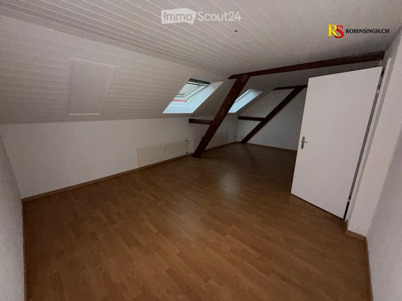 Empty attic room with wooden flooring, white walls, exposed wooden beams, and skylight windows.
