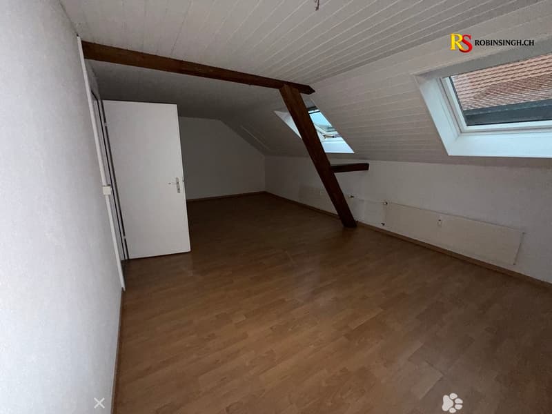 Empty attic room with wooden flooring, white walls, and skylight windows.
