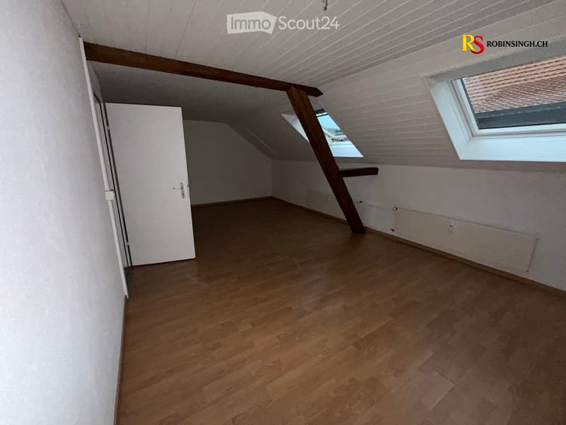 Empty attic room with wooden flooring, white walls, and skylight windows.